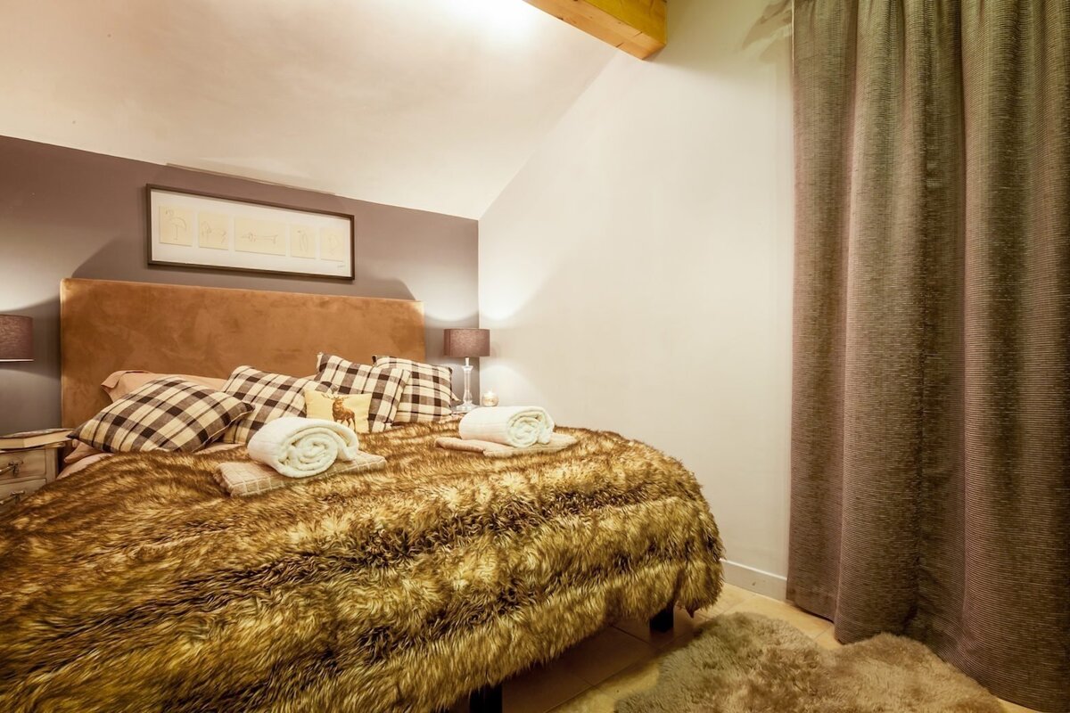 A cozy, rustic bedroom features a bed with a fluffy brown faux fur blanket and plaid pillows. Warm tones and inviting decor.