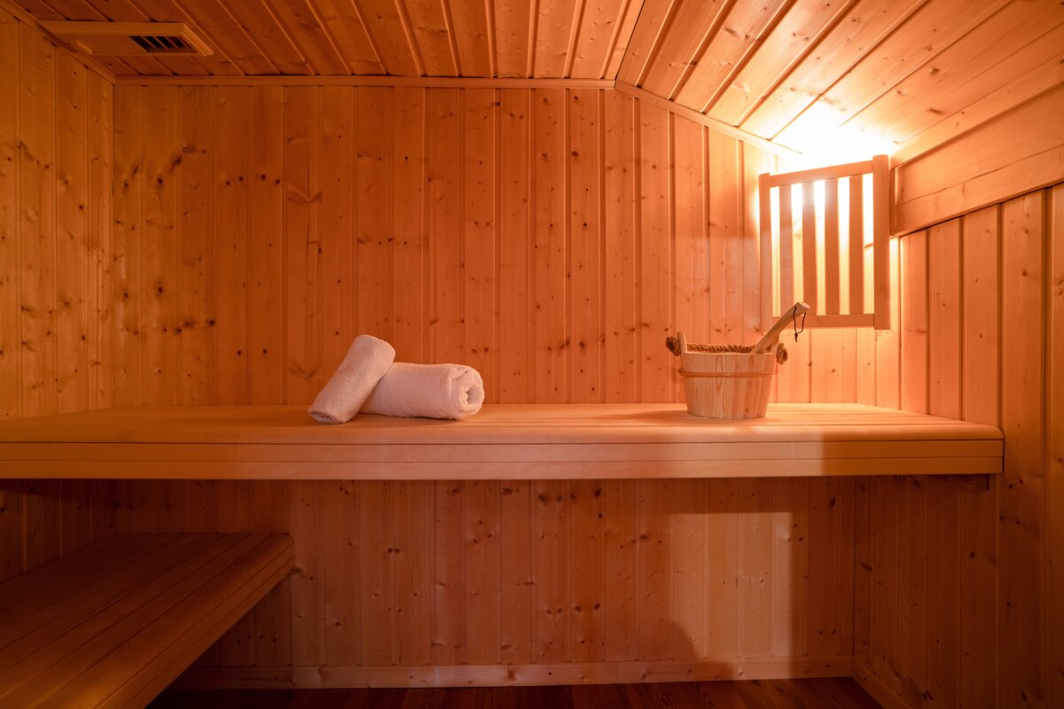A warm, inviting wooden sauna with two white rolled towels, a wooden bucket and ladle on the bench, illuminated by a soft light.