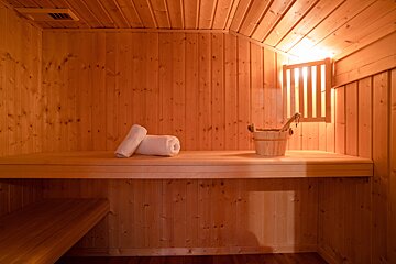 A warm, inviting wooden sauna with two white rolled towels, a wooden bucket and ladle on the bench, illuminated by a soft light.