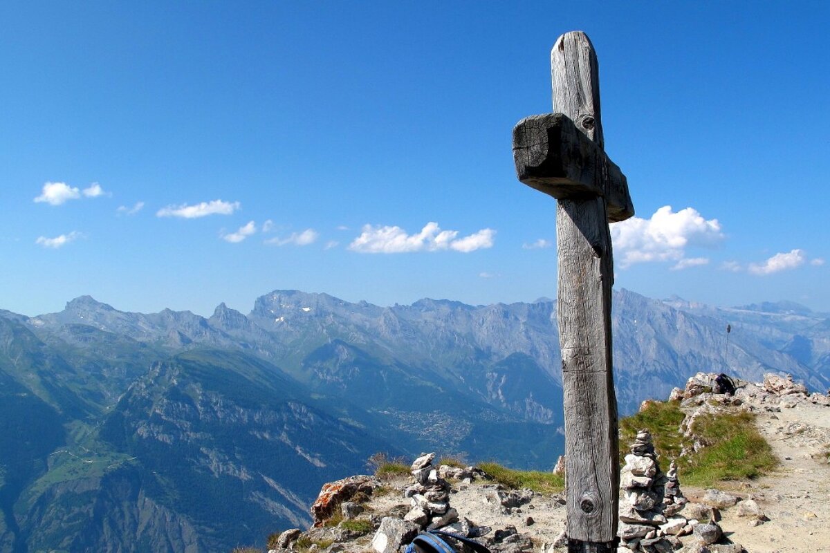 A wooden cross on top of a mountain with mountains in the background