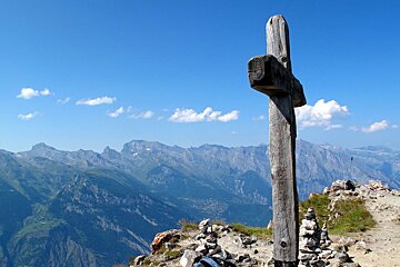 A wooden cross on top of a mountain with mountains in the background