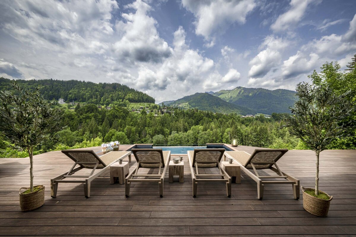 A deck with chairs and a swimming pool with mountains in the background