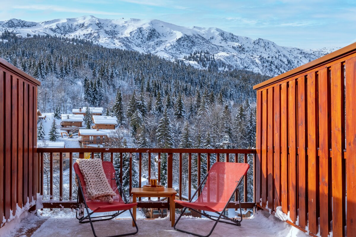 A balcony with two chairs and a table with mountains in the background