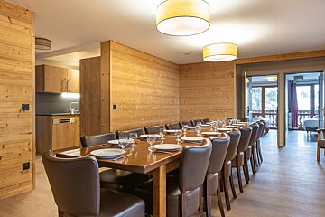 A long wooden dining table set for a group, surrounded by brown leather chairs in a cozy, wood-paneled chalet interior.
