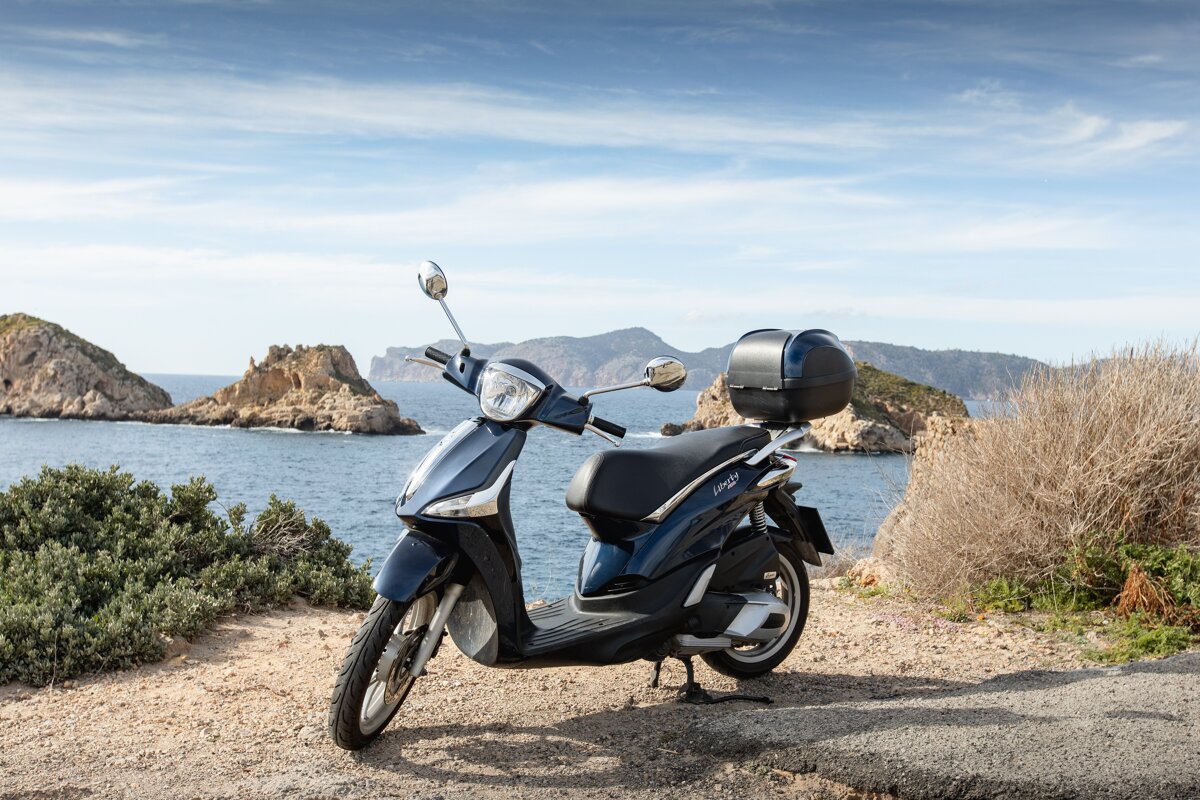 A scooter is parked on the side of a road near the ocean