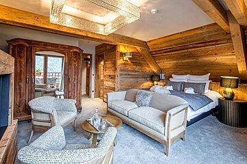A rustic alpine bedroom featuring a large bed, seating area with sofa, and wooden paneling.