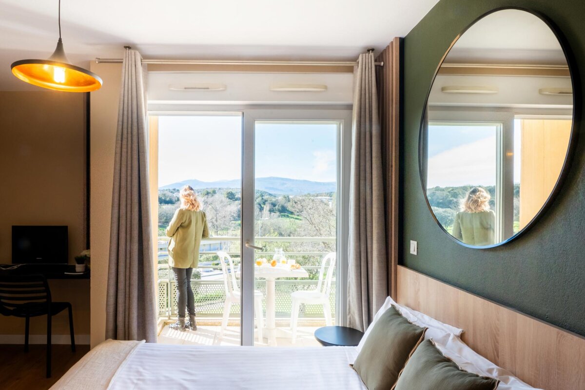 A woman standing in a hotel room looking out a window