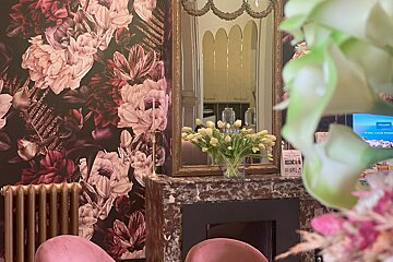 A vase of flowers sits on a fireplace in front of a mirror