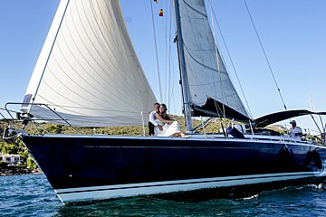 A bride and groom pose on a sailboat in the ocean