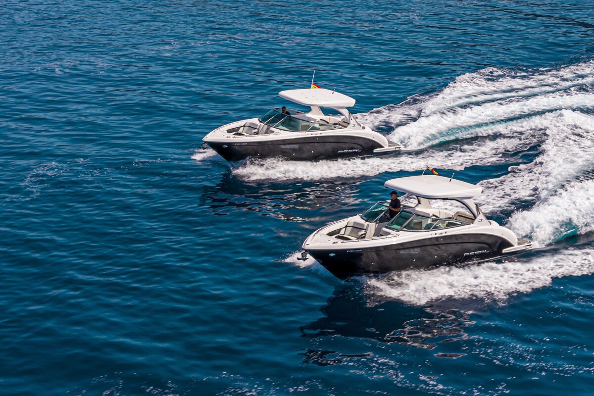Two black and white motorboats cruise side-by-side on deep blue water, leaving white wakes in their path.