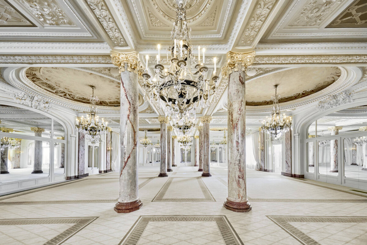 A hallway with columns and chandeliers hanging from the ceiling