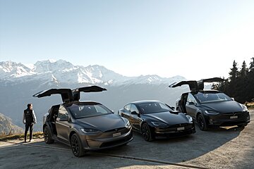 Three Tesla cars (two Model X with open falcon doors, one Model S) are parked on a mountain road with snowy peaks in the background. A person stands by one car.