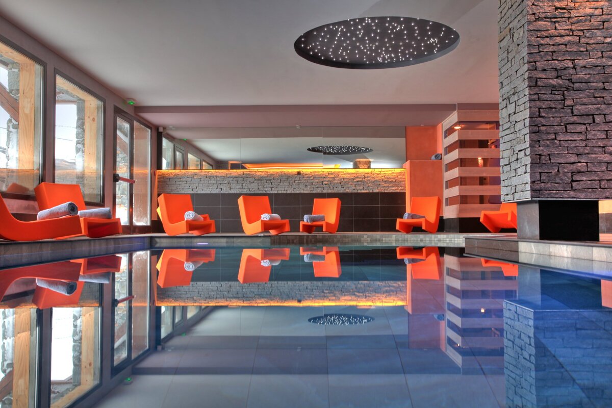 A large indoor swimming pool with orange chairs and a starry ceiling