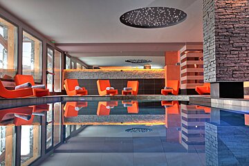 A large indoor swimming pool with orange chairs and a starry ceiling