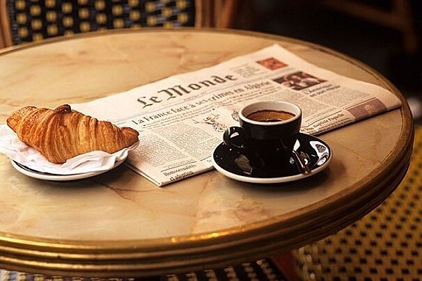 A croissant and a cup of coffee on a table with a newspaper that says le monde