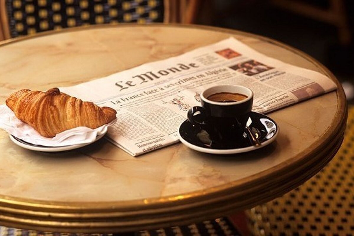 A croissant and a cup of coffee on a table with a newspaper that says le monde