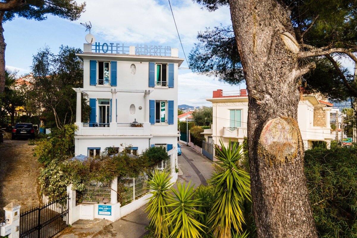A white building with blue shutters has the word hotel on top