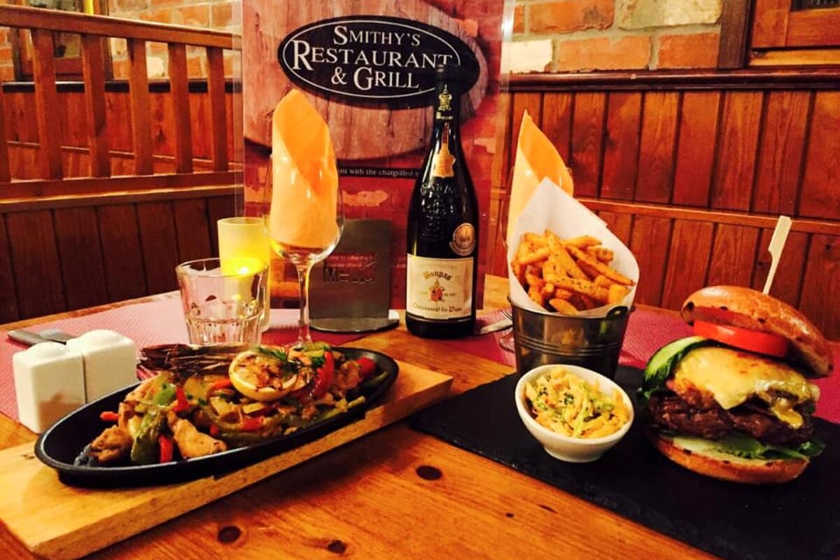 A restaurant meal featuring a cheeseburger, fries, and sizzling fajitas, alongside wine and candlelight, at Smithy's Restaurant & Grill.