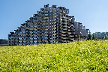 A large building with many balconies sits in the middle of a grassy field