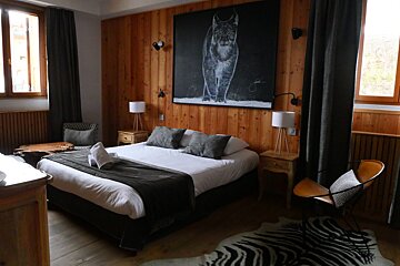 A rustic-modern bedroom features a large lynx painting on a wood-paneled wall, a bed with dark linens, and a striking zebra print rug.