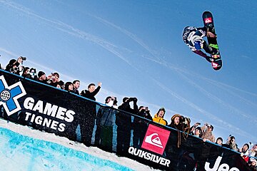 A snowboarder is doing a trick in the air at the games tignes
