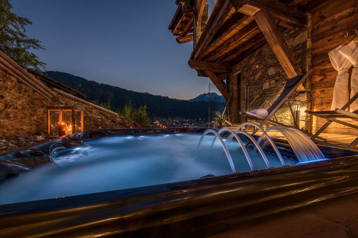 A hot tub with mountains in the background is lit up at night