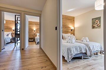 A bright hallway leads to several modern bedrooms, each featuring wooden accent walls and beds. The room on the right has twin beds with robes and a fox picture.
