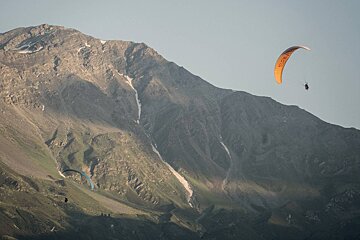 A person is parasailing in front of a mountain with a parachute that says ' sss ' on it