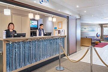 A man and a woman are at a hotel reception desk