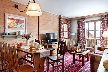 Warm mountain chalet interior with wood-paneled walls, a red plaid carpet, a dining table set, and cozy armchairs.