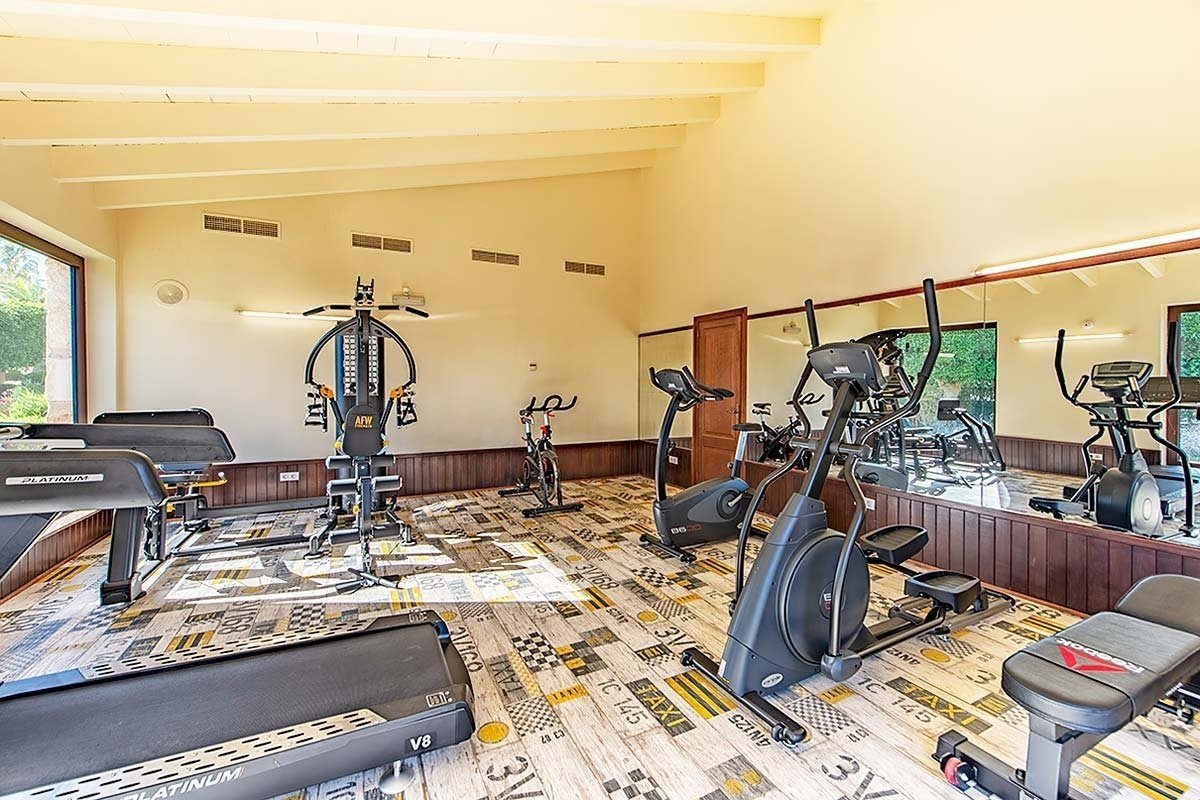 A well-equipped gym with treadmills, ellipticals, a multi-gym, and bikes, featuring unique taxi-patterned flooring and large mirrors.