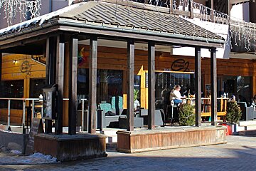 A man sits at a table in front of a building that says ' le bistro ' on it