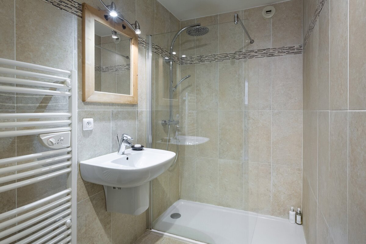 A neutral-toned bathroom with a walk-in shower, wall-mounted sink, wooden mirror, and a white heated towel rail.