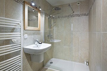 A neutral-toned bathroom with a walk-in shower, wall-mounted sink, wooden mirror, and a white heated towel rail.