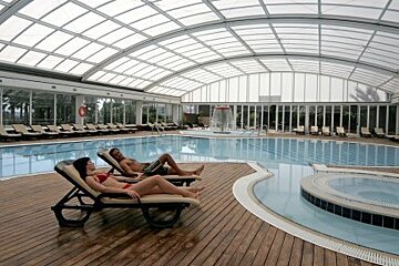 A man and a woman are laying on lounge chairs near a large indoor swimming pool