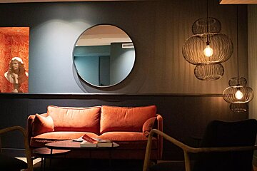 A living room with an orange couch and a round mirror