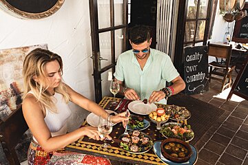 A man and woman sit at a table with plates of food and a sign that says quality over quantity