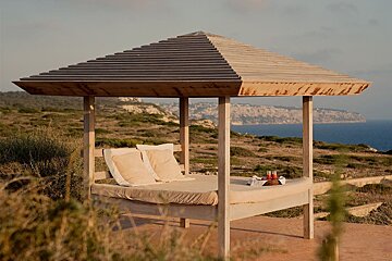 A gazebo with a bed underneath it overlooking the ocean
