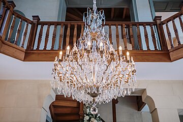 A large crystal chandelier hangs from a wooden staircase