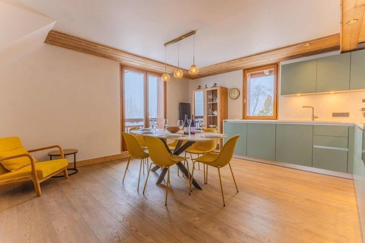 Bright open-plan kitchen and dining area featuring a dining table with yellow chairs and light green cabinets.