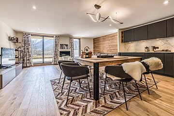 Spacious, modern open-plan living room and kitchen with sleek design, wooden elements, a dining area, and stunning mountain views.