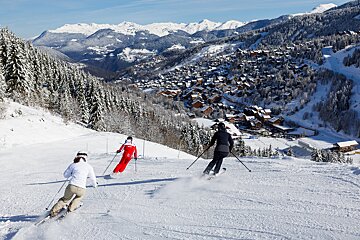 Three people skiing down a snowy slope with mountains in the background