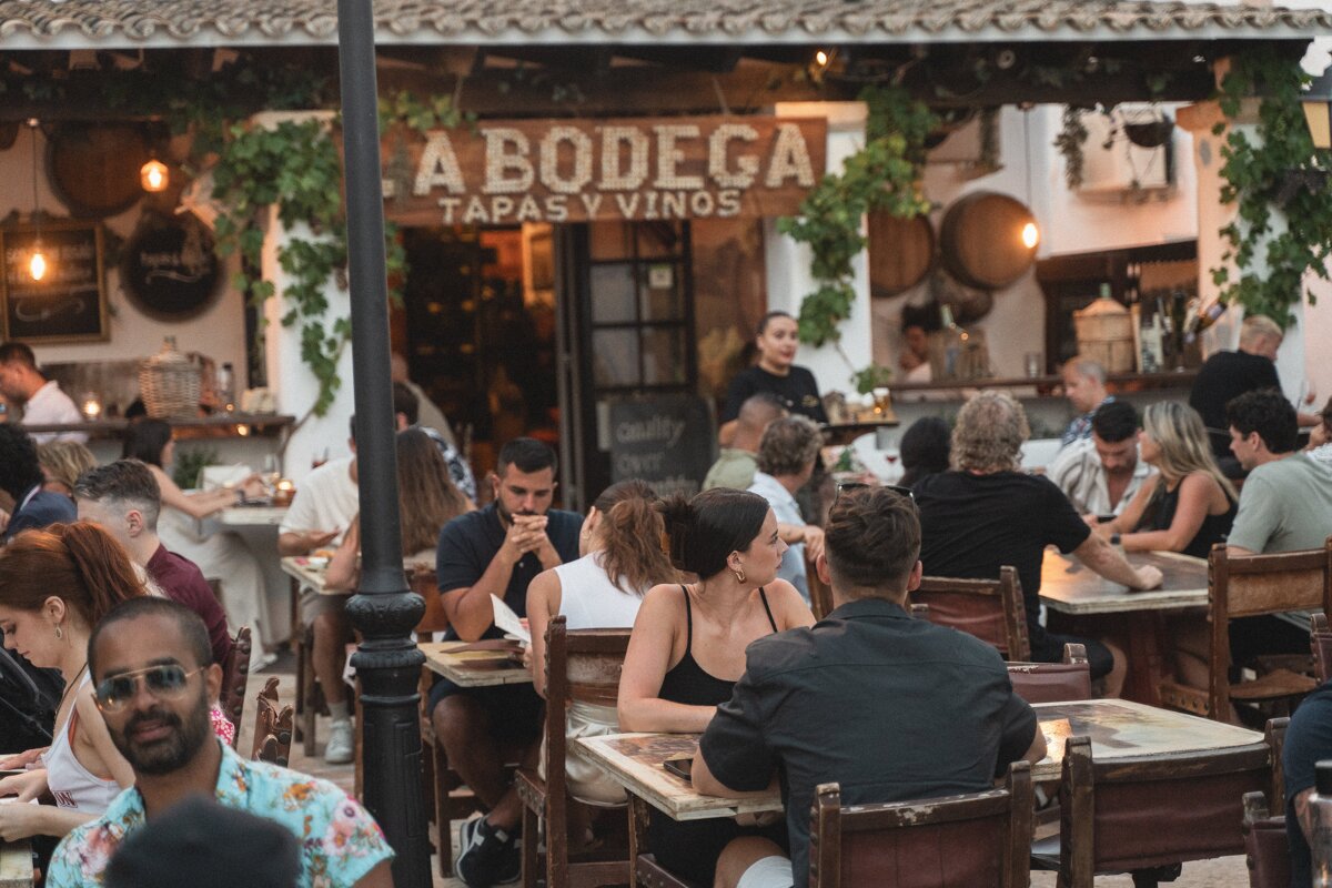 A group of people sit at tables outside a bodega tapas y vinos restaurant