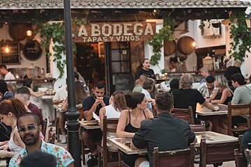 A group of people sit at tables outside a bodega tapas y vinos restaurant