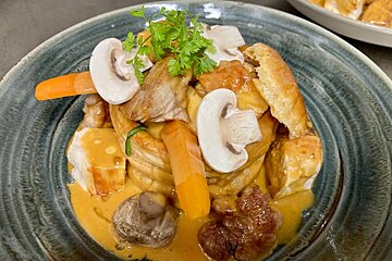 A savory vol-au-vent filled with chicken, mushrooms, and carrots in a rich creamy sauce, garnished with fresh herbs on a rustic plate.