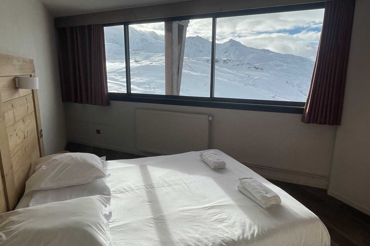 A bedroom with a bed and a window with mountains in the background