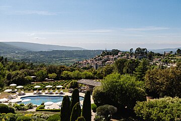 A large swimming pool surrounded by chairs and umbrellas with a village in the background