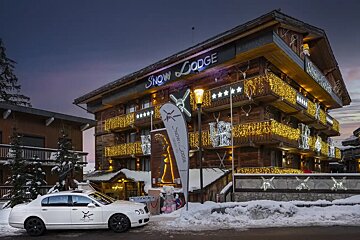 A white car is parked in front of a snow lodge