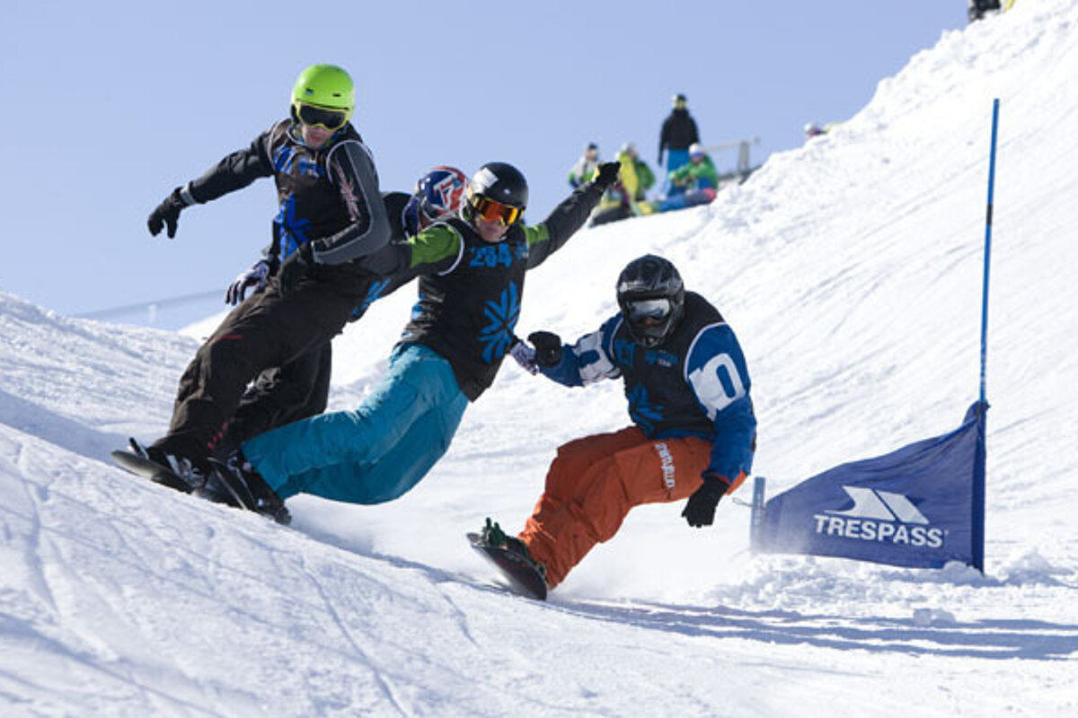 Three snowboarders are going down a snowy slope next to a trespass flag
