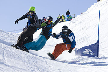 Three snowboarders are going down a snowy slope next to a trespass flag